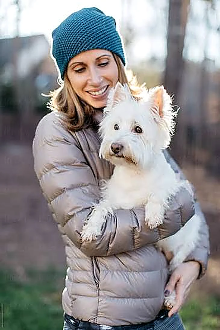 Sarah, owner of Sarah’s Dog Grooming, smiling while holding up a freshly groomed puppy